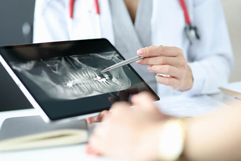 Dentist shows an X-ray of jaw to patient on tablet.