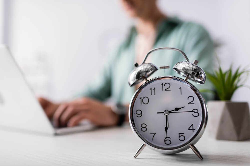 Selective focus of alarm clock on table near man using laptop at home