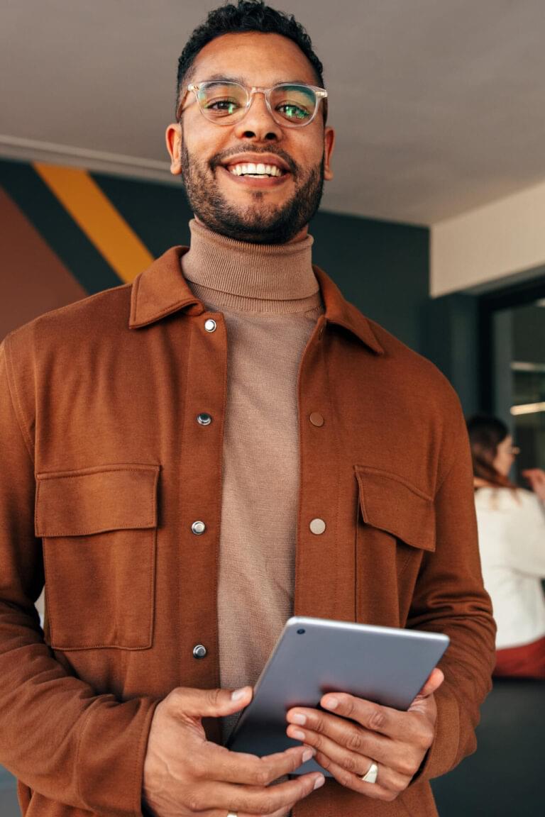 Happy young businessman looking at the camera while holding a digital tablet