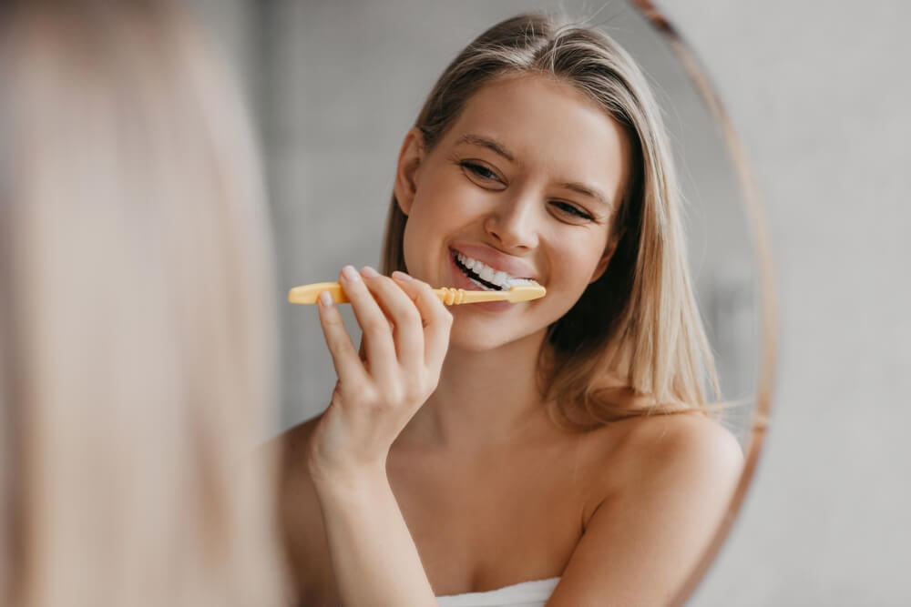 Young woman brushing teeth with toothbrush and looking in mirror