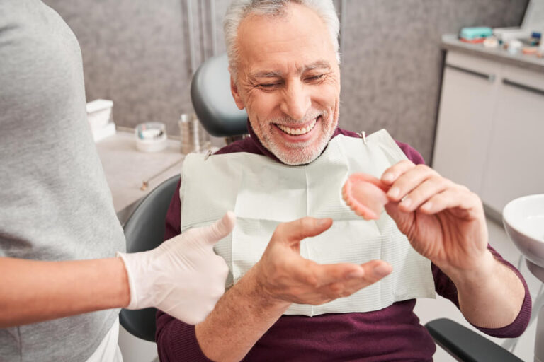 dentist showing to senior grey haired patient teeth dentures