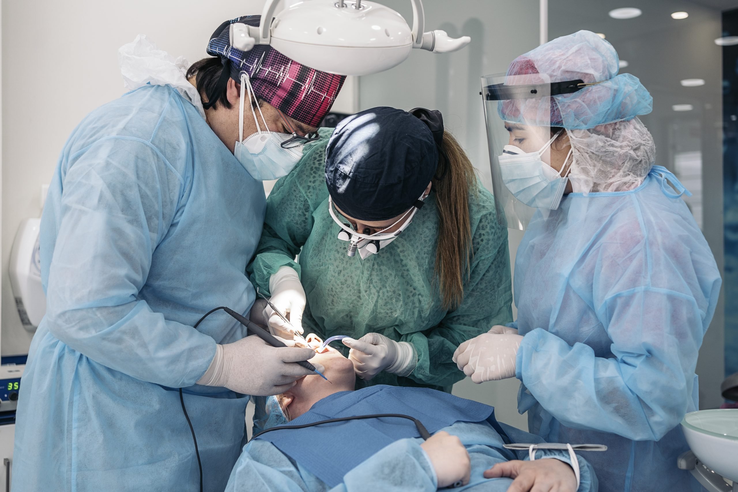 Dentist wearing face mask and dental magnifying glasses doing treatment to unrecognized patient.